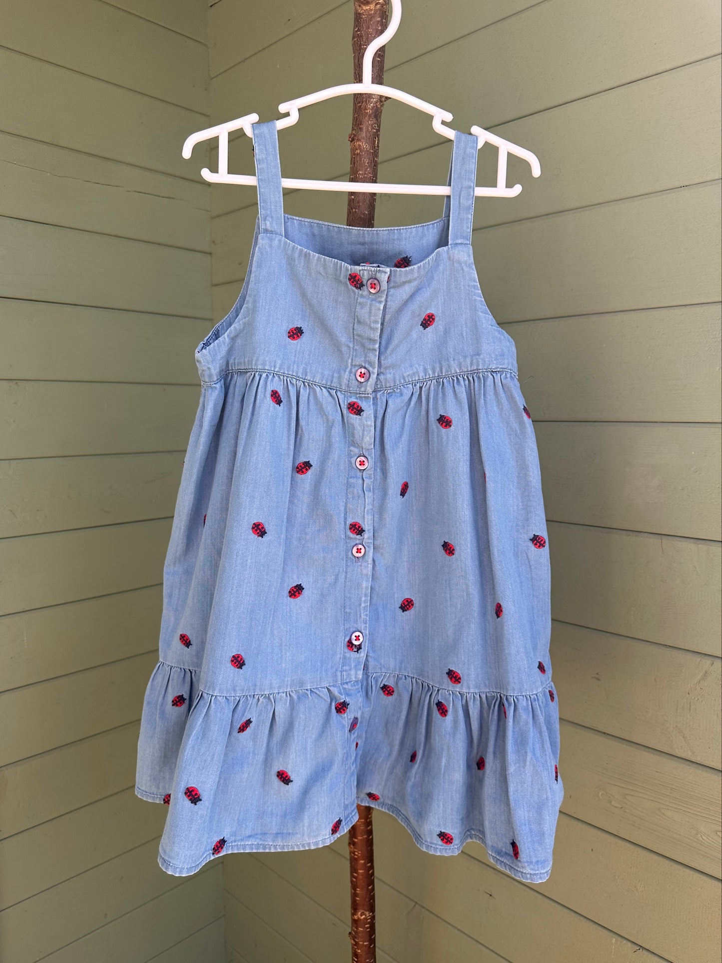 Light blue dress with red ladybirds on a hanger against a wooden wall.