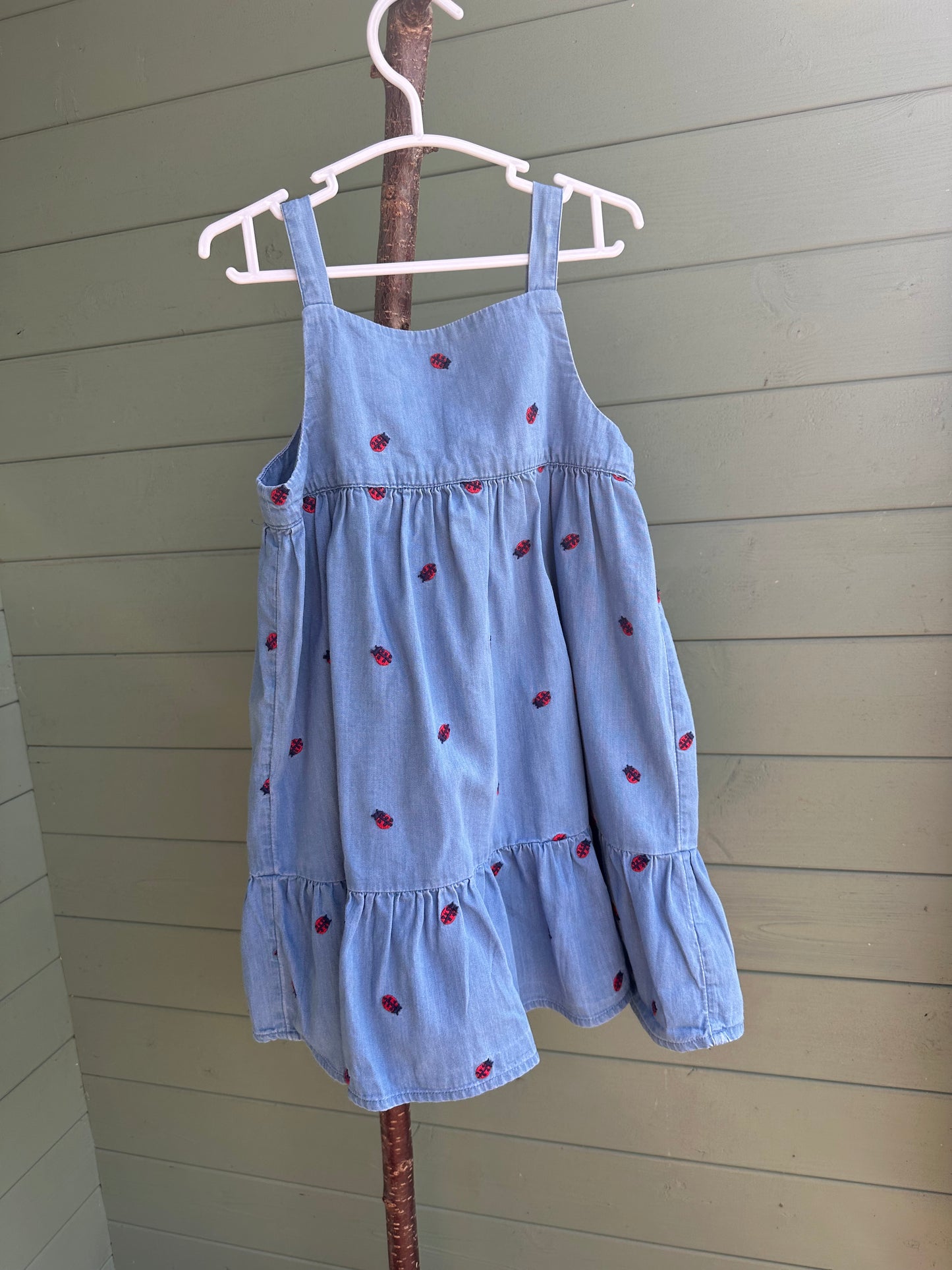 Light blue dress with red polka dots on a hanger against a wooden wall.