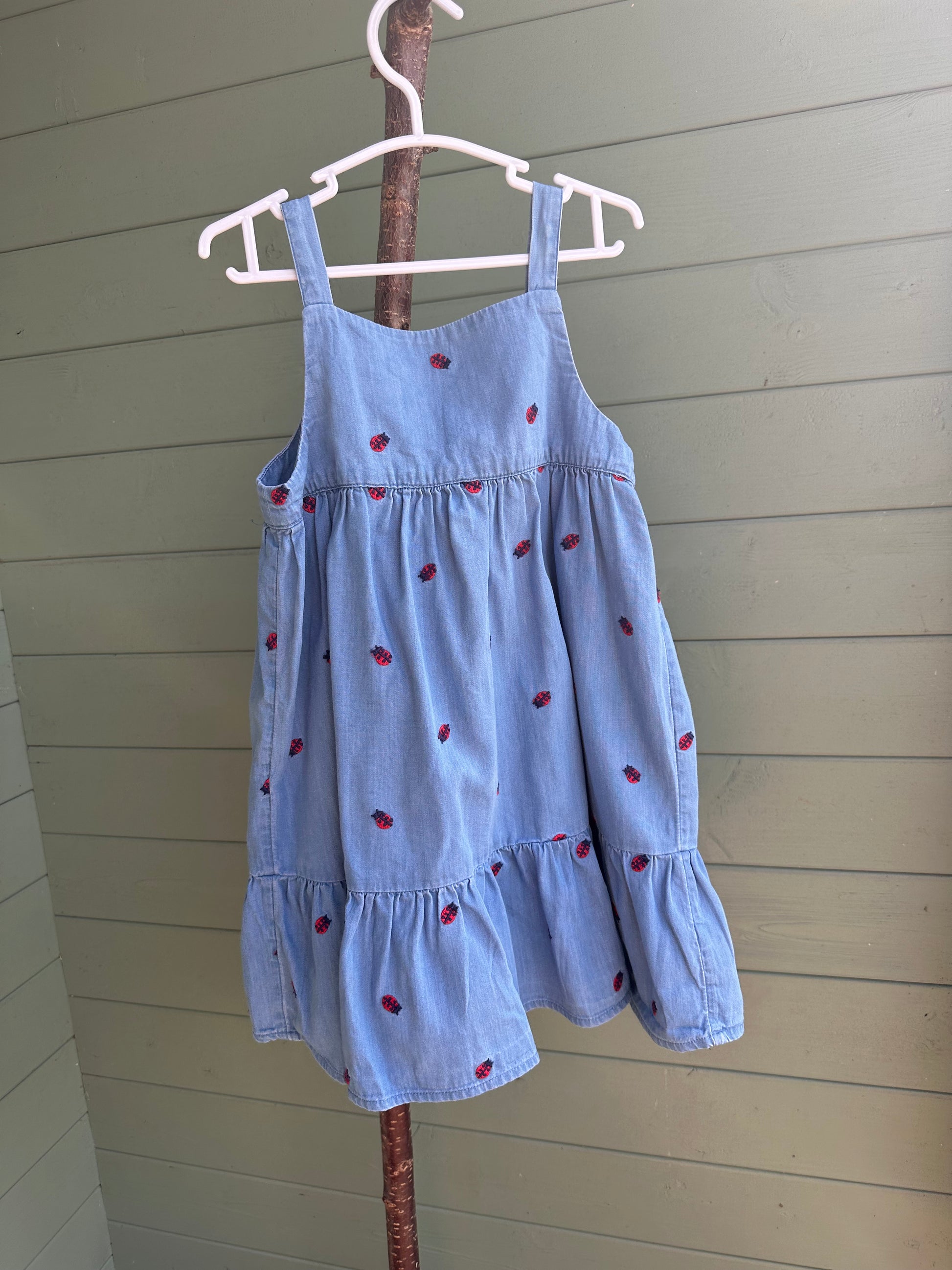 Light blue dress with red polka dots on a hanger against a wooden wall.