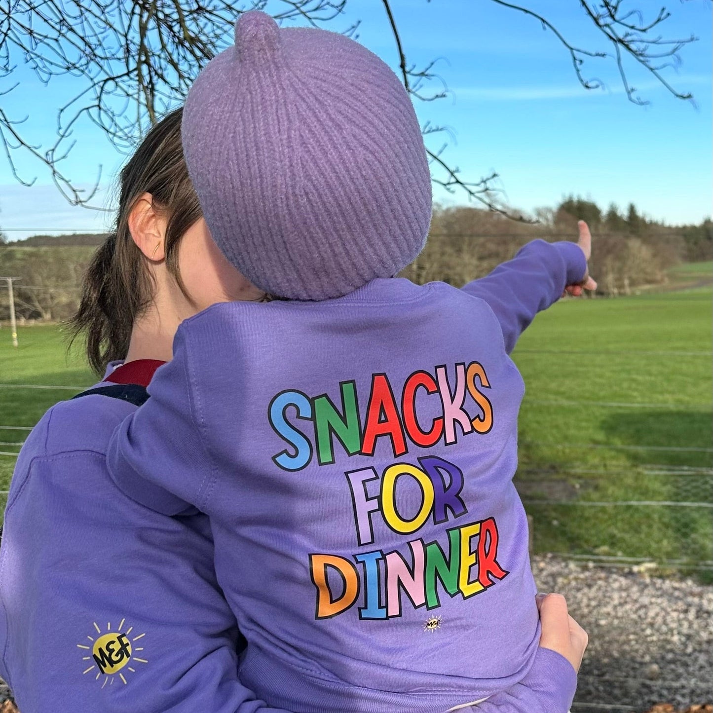 Purple sweater 'SNACKS FOR DINNER' text outdoors
