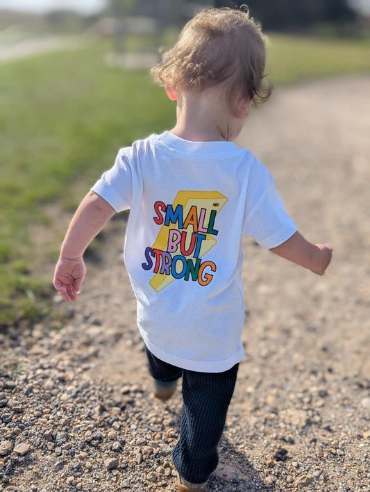 Child wearing a white t-shirt with 'Small But Strong' text, running outdoors.