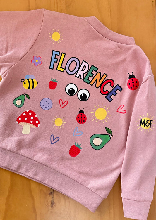 Pink sweatshirt with colorful graphics and 'FLORENCE' text on a wooden surface