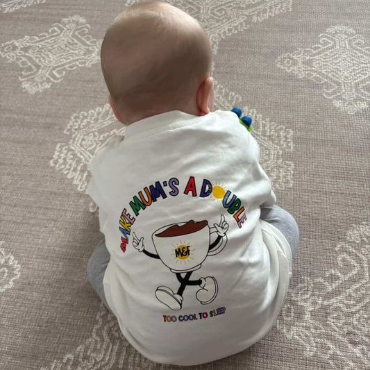 Baby wearing a onesie with text and graphics on a patterned carpet